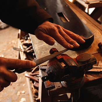 Dettaglio delle mani di un artigiano intento a limare un oggetto metallico fissato da una morsa